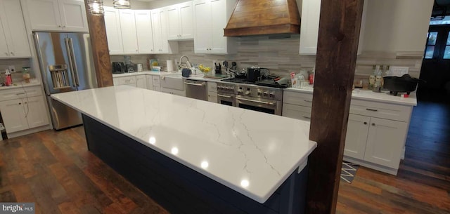 kitchen with dark wood-type flooring, stainless steel appliances, premium range hood, backsplash, and white cabinets