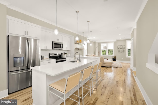 kitchen with a kitchen island with sink, white cabinets, a kitchen breakfast bar, appliances with stainless steel finishes, and decorative light fixtures