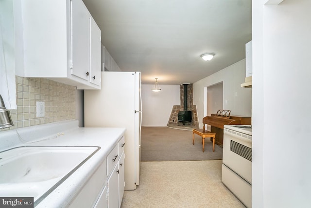 kitchen with tasteful backsplash, white appliances, pendant lighting, white cabinets, and a wood stove