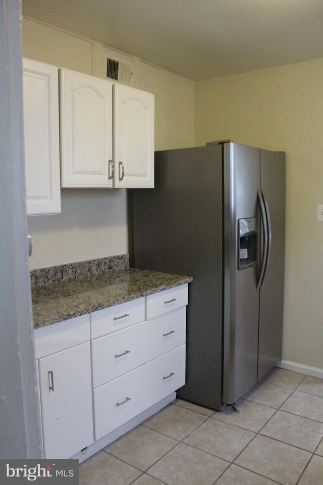 kitchen featuring stainless steel fridge, white cabinets, dark stone counters, and light tile patterned floors