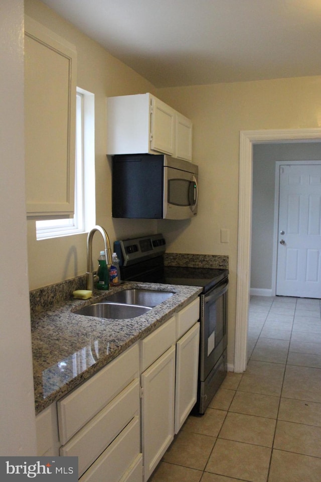 kitchen with white cabinetry, sink, dark stone counters, light tile patterned floors, and appliances with stainless steel finishes