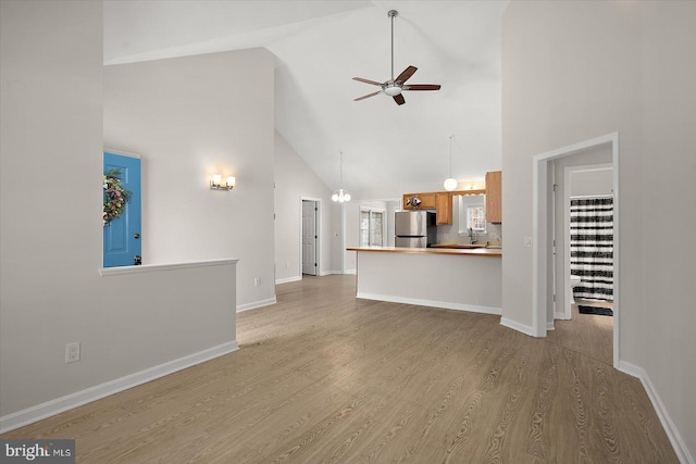 unfurnished living room with high vaulted ceiling, ceiling fan, baseboards, and wood finished floors