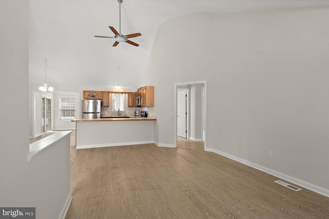 unfurnished living room with baseboards, visible vents, ceiling fan, light wood-type flooring, and high vaulted ceiling