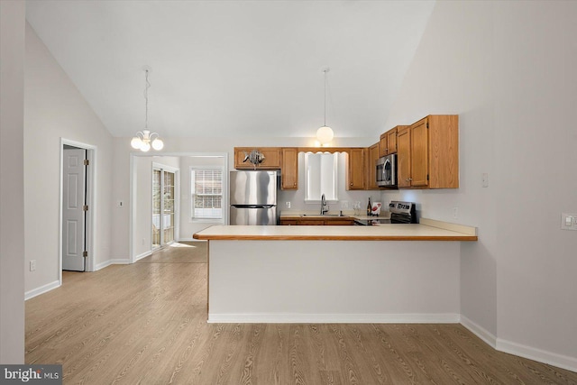 kitchen featuring a peninsula, appliances with stainless steel finishes, a sink, and light wood-style flooring