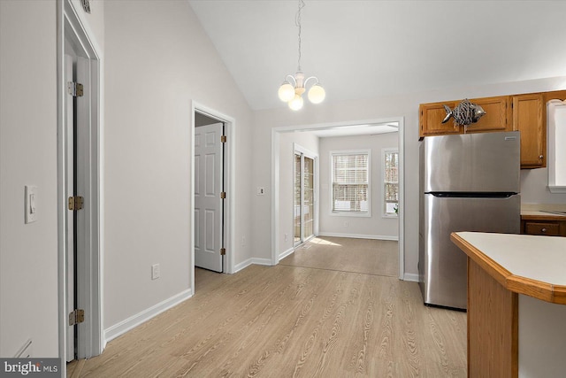 kitchen featuring light countertops, light wood-style flooring, brown cabinetry, freestanding refrigerator, and vaulted ceiling