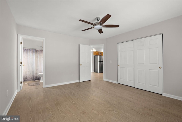 unfurnished bedroom with a closet, baseboards, wood finished floors, and freestanding refrigerator