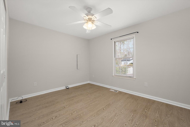 empty room with a ceiling fan, visible vents, baseboards, and wood finished floors