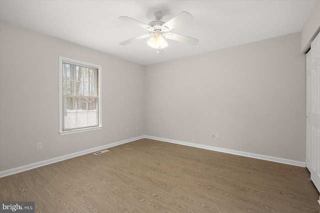 empty room with a ceiling fan, visible vents, baseboards, and wood finished floors