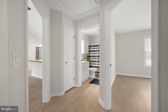 hallway with light wood-style floors, attic access, and baseboards