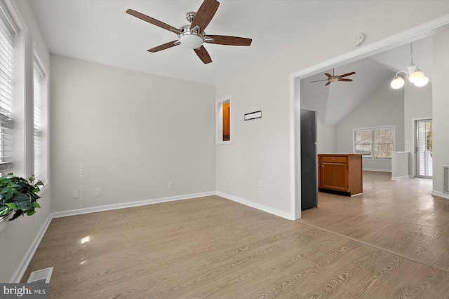 unfurnished room with vaulted ceiling, ceiling fan with notable chandelier, light wood-style flooring, and baseboards