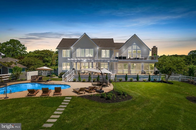 back house at dusk with a patio area, a balcony, a fenced in pool, and a yard