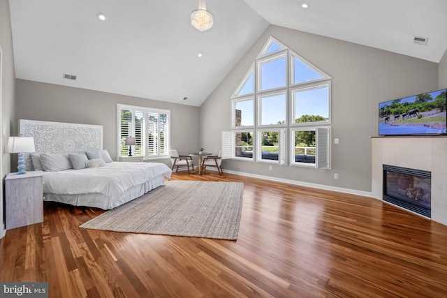 bedroom with wood-type flooring, high vaulted ceiling, and a tiled fireplace