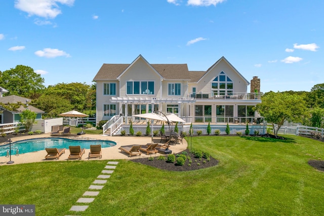 rear view of property featuring a yard, a balcony, a patio, and a fenced in pool