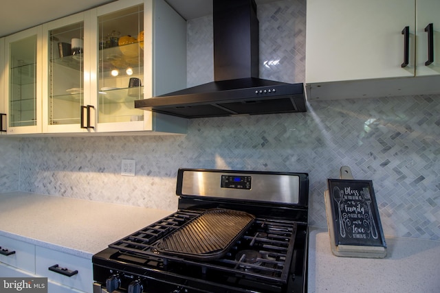 kitchen with tasteful backsplash, white cabinets, black gas stove, and wall chimney exhaust hood