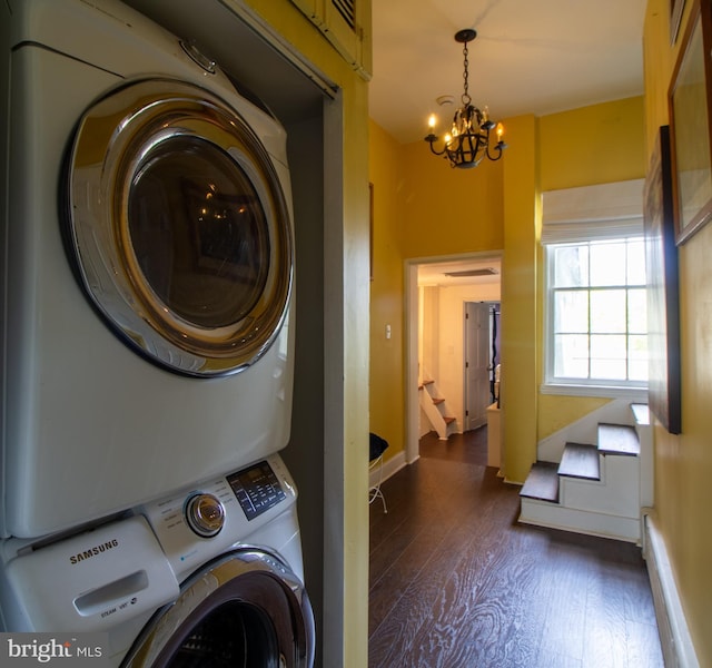 clothes washing area featuring dark hardwood / wood-style floors, stacked washer / dryer, a baseboard radiator, and a chandelier