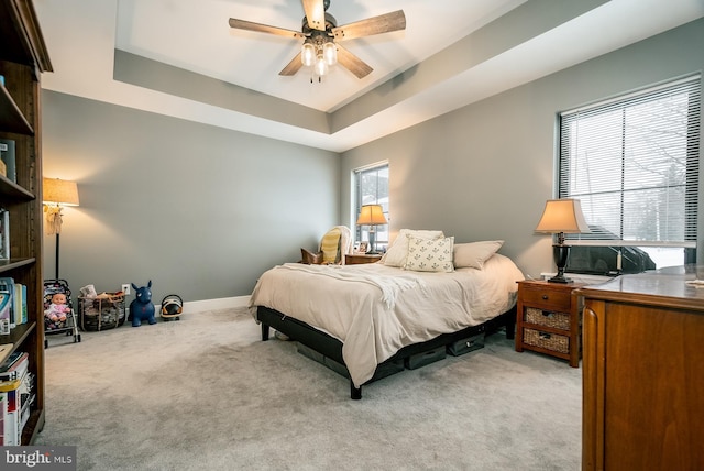 bedroom featuring a raised ceiling, ceiling fan, and light colored carpet