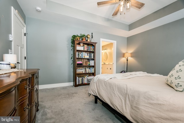 carpeted bedroom with ceiling fan, a tray ceiling, and ensuite bathroom