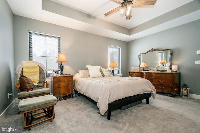 carpeted bedroom with multiple windows, a raised ceiling, and ceiling fan