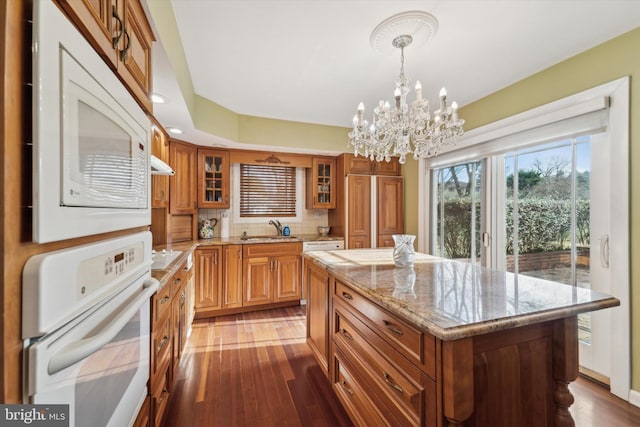 kitchen featuring pendant lighting, a center island, white appliances, dark wood-type flooring, and a chandelier