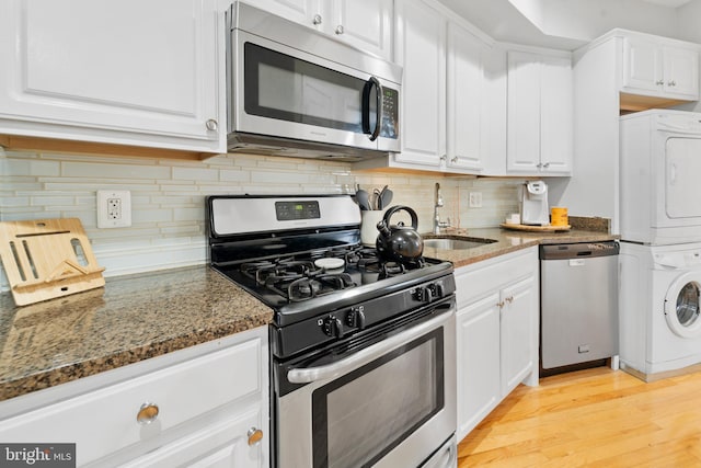 kitchen featuring dark stone counters, white cabinets, stacked washer and dryer, light wood-type flooring, and stainless steel appliances