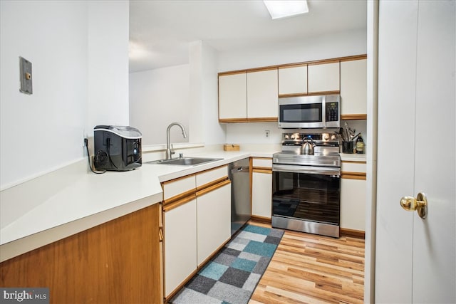 kitchen with light wood-type flooring, appliances with stainless steel finishes, white cabinetry, and sink