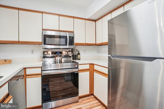 kitchen with appliances with stainless steel finishes, light hardwood / wood-style floors, and white cabinetry