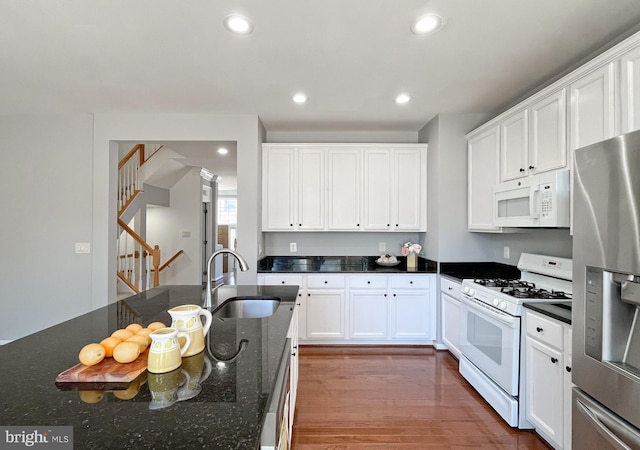 kitchen featuring dark stone counters, white appliances, sink, hardwood / wood-style flooring, and white cabinets