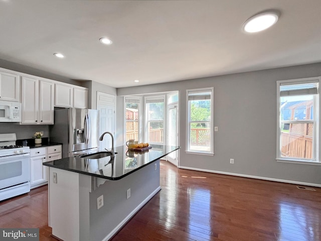 kitchen featuring white appliances, dark wood-type flooring, a center island with sink, sink, and white cabinetry