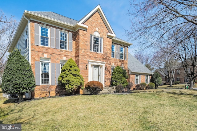 view of front facade with brick siding, a shingled roof, and a front lawn