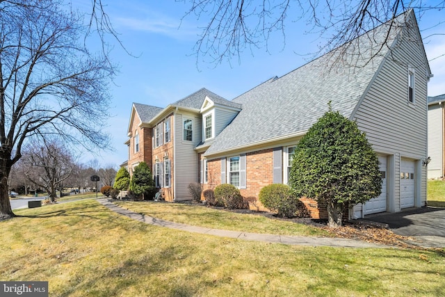 view of front facade with brick siding, driveway, a front lawn, and roof with shingles