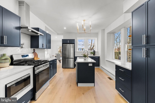 kitchen featuring a center island, backsplash, wall chimney range hood, appliances with stainless steel finishes, and a chandelier