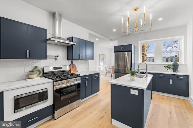 kitchen with sink, wall chimney exhaust hood, an inviting chandelier, a center island with sink, and appliances with stainless steel finishes