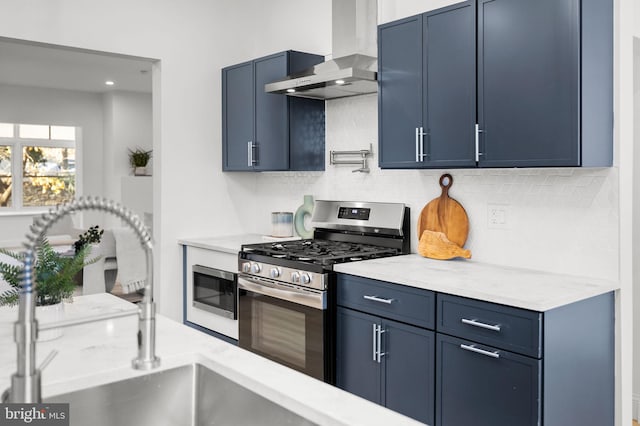 kitchen with sink, wall chimney exhaust hood, stainless steel appliances, and blue cabinets