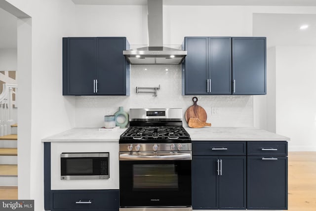 kitchen featuring light stone counters, range hood, decorative backsplash, appliances with stainless steel finishes, and light wood-type flooring