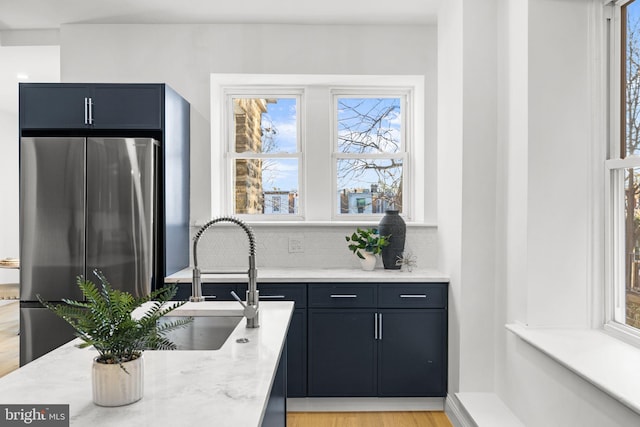 kitchen with backsplash, sink, light hardwood / wood-style flooring, stainless steel fridge, and light stone counters