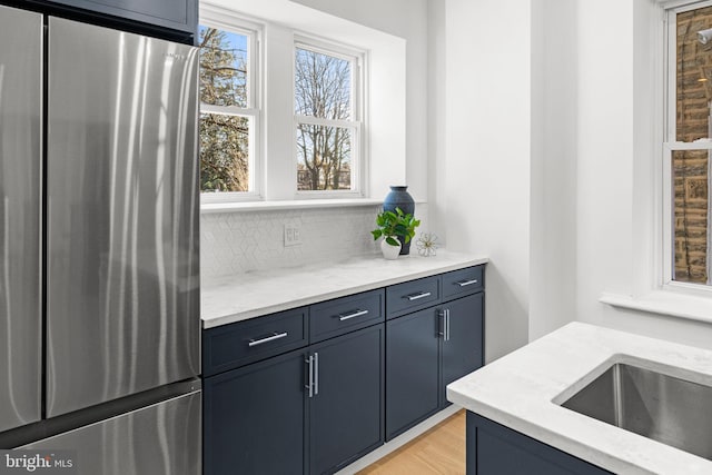 kitchen with decorative backsplash, light wood-type flooring, sink, and stainless steel refrigerator