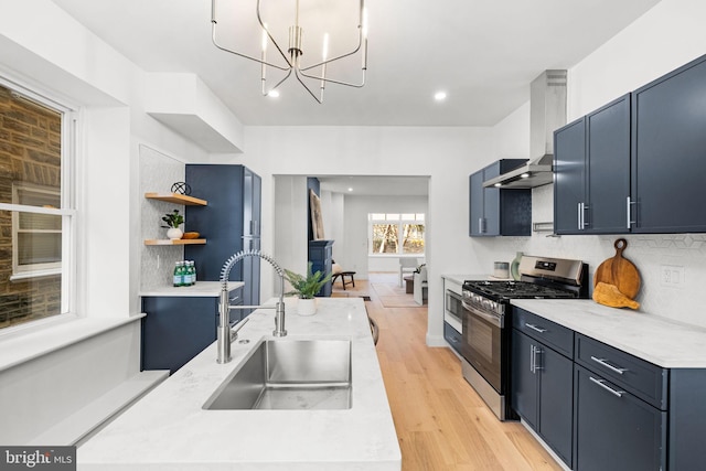 kitchen with sink, wall chimney exhaust hood, stainless steel gas range, pendant lighting, and light wood-type flooring