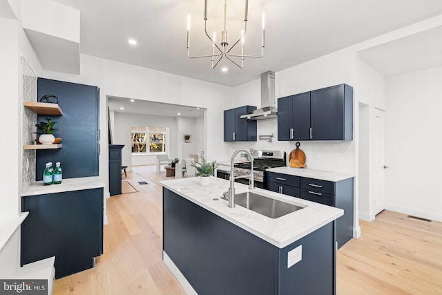 kitchen with sink, wall chimney exhaust hood, blue cabinetry, light hardwood / wood-style floors, and a chandelier