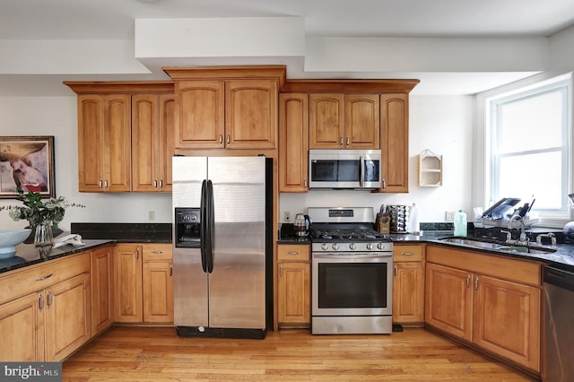 kitchen featuring dark stone counters, sink, stainless steel appliances, and light hardwood / wood-style flooring