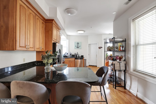 kitchen with a kitchen bar, dark stone countertops, light hardwood / wood-style flooring, and appliances with stainless steel finishes