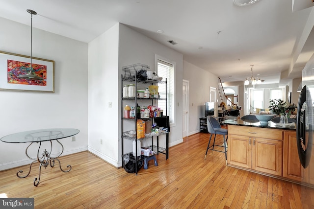 kitchen featuring stainless steel refrigerator with ice dispenser, decorative light fixtures, light hardwood / wood-style flooring, a notable chandelier, and a kitchen bar