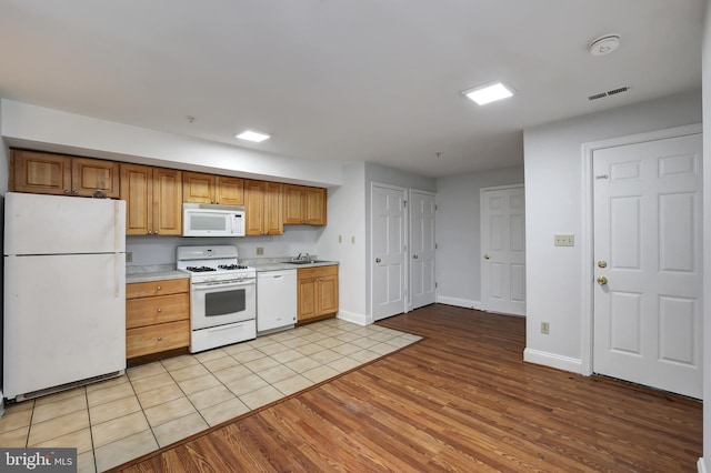 kitchen with light wood-type flooring, white appliances, and sink