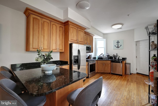 kitchen with dark stone counters, light hardwood / wood-style flooring, a kitchen bar, kitchen peninsula, and stainless steel appliances