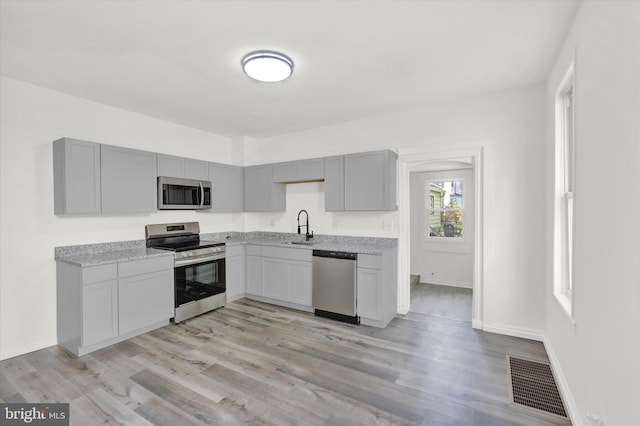 kitchen with gray cabinets, sink, stainless steel appliances, and light wood-type flooring