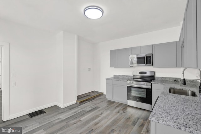 kitchen with gray cabinetry, light stone countertops, sink, light hardwood / wood-style flooring, and appliances with stainless steel finishes