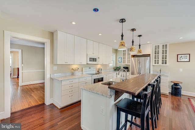 kitchen featuring sink, white appliances, white cabinetry, a center island with sink, and decorative light fixtures