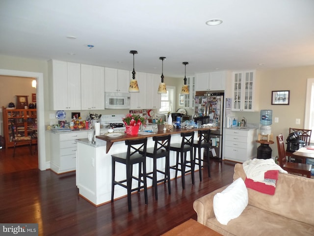 kitchen featuring a breakfast bar, white appliances, pendant lighting, a center island with sink, and white cabinetry