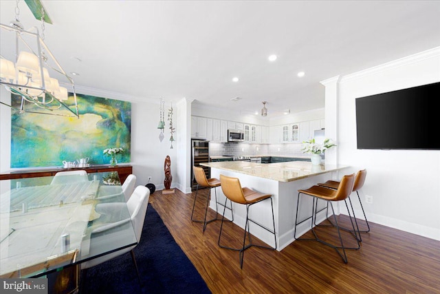 kitchen with kitchen peninsula, dark hardwood / wood-style flooring, tasteful backsplash, white cabinetry, and a breakfast bar area