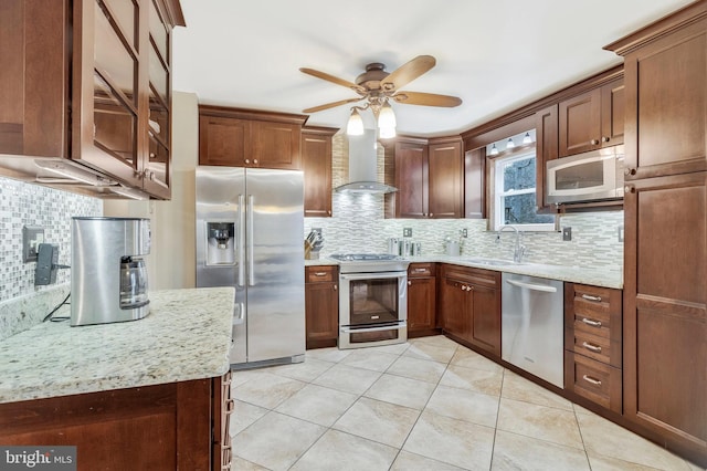 kitchen featuring light stone countertops, ceiling fan, sink, wall chimney exhaust hood, and stainless steel appliances