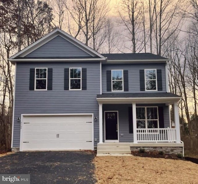 traditional home featuring an attached garage, covered porch, and aphalt driveway